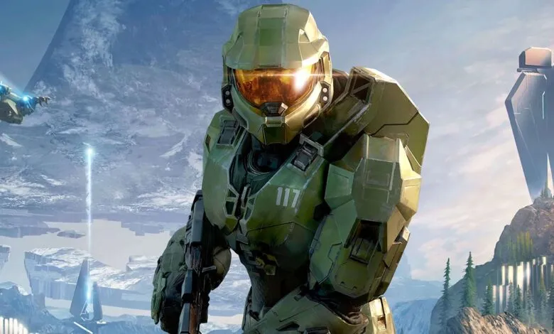 Master Chief in his iconic green armor stands ready with a weapon, overlooking a vast alien landscape.