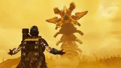 A Helldiver faces a giant, monstrous worm in a desolate, yellow landscape.