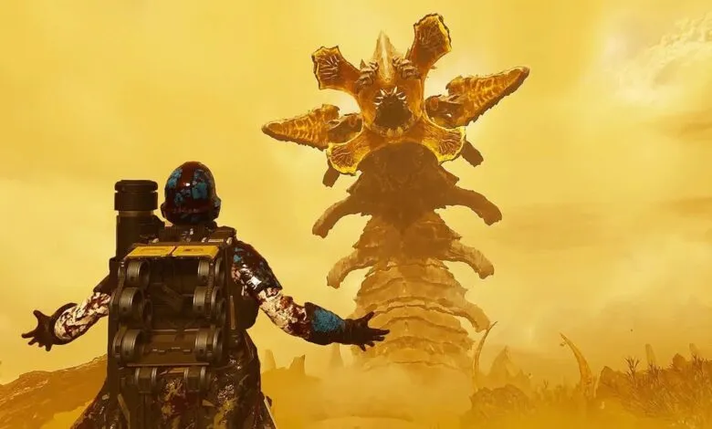 A Helldiver faces a giant, monstrous worm in a desolate, yellow landscape.