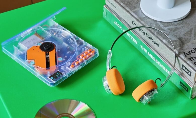 Transparent portable CD player with orange accents and headphones on a green surface.