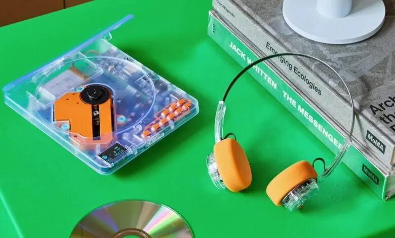 Transparent portable CD player with orange accents and headphones on a green surface.