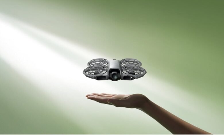 A compact, white drone with protective propeller guards hovers above an open palm.