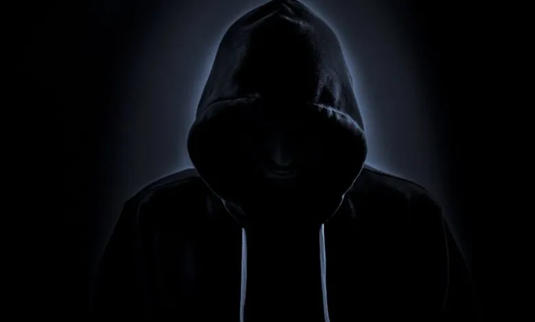 Person wearing a dark hooded sweatshirt, face obscured by shadow.