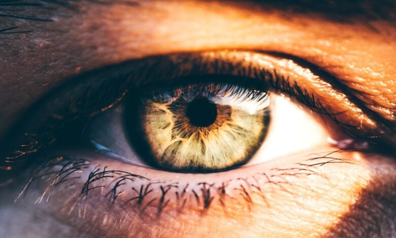 Extreme close-up of a human eye with green and brown iris, detailed skin texture, and eyelashes.
