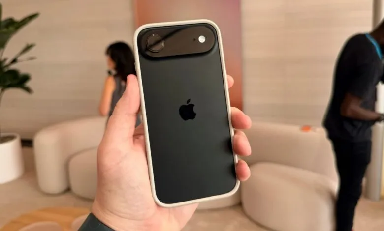 Hand holding a black iPhone with a white case, showing the Apple logo and camera module.