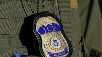 Close-up of an ICE Officer badge hanging from a chain on a tactical vest.