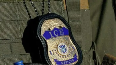 Close-up of an ICE Officer badge hanging from a chain on a tactical vest.