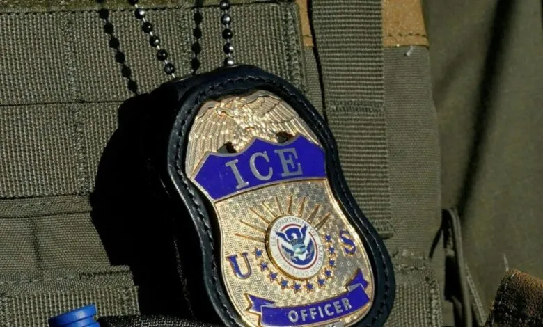 Close-up of an ICE Officer badge hanging from a chain on a tactical vest.