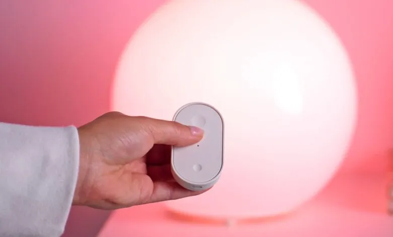 Hand holding a small white remote control in front of a large, glowing orb lamp.