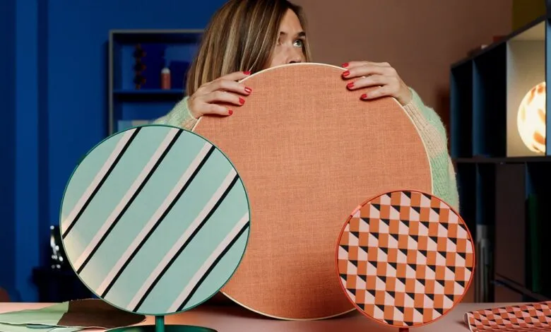 Woman holds three round, patterned acoustic panels in a colorful room.