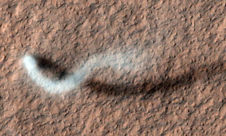 A white plume of dust or gas trails across the reddish-brown surface of Mars.