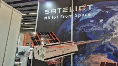 A model satellite with solar panels is displayed at a trade show booth.