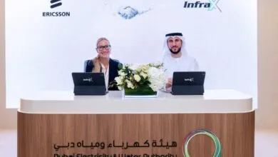Two individuals, a woman and a man in traditional attire, sit at a table with laptops, smiling.