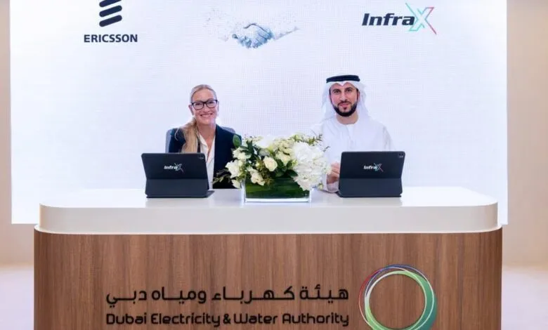 Two individuals, a woman and a man in traditional attire, sit at a table with laptops, smiling.