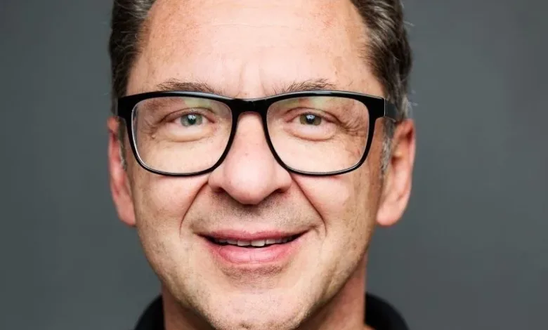 Close-up portrait of a smiling man with glasses and dark hair.