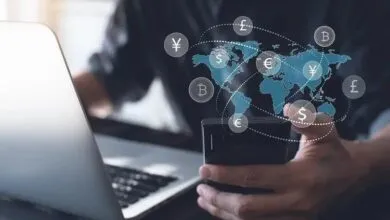 Person using a smartphone and laptop with a global currency exchange graphic overlay.