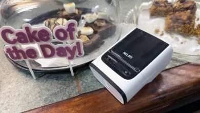 A white and black receipt printer sits next to a glass dome displaying brownies.