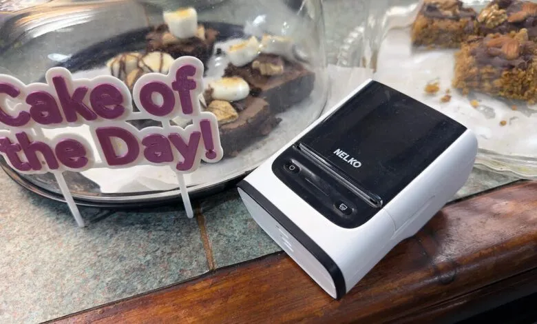 A white and black receipt printer sits next to a glass dome displaying brownies.