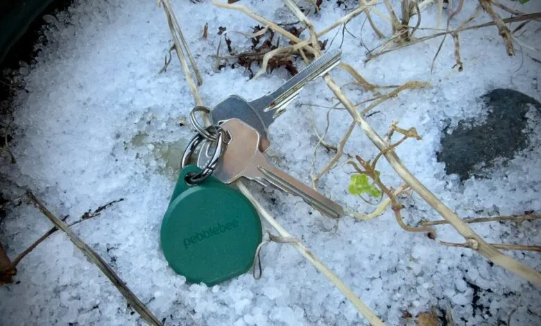Keys with Pebblebee tracker on ground covered in hail.