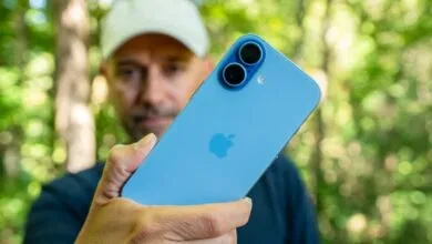 Man holding a blue iPhone with dual rear cameras outdoors.