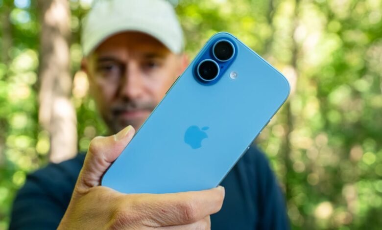 Man holding a blue iPhone with dual rear cameras outdoors.
