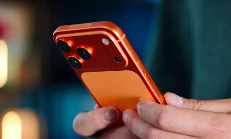 Close-up of an orange smartphone being held, focusing on the camera array.