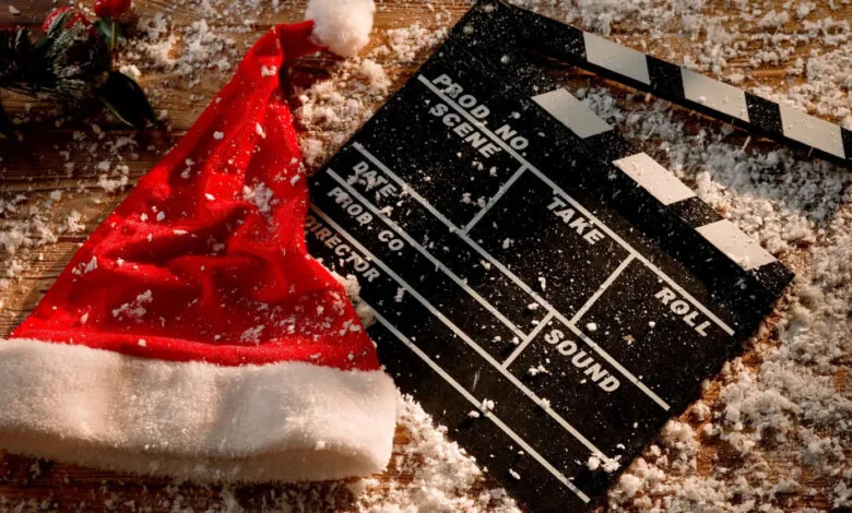 A festive clapperboard and Santa hat dusted with snow on a wooden surface.