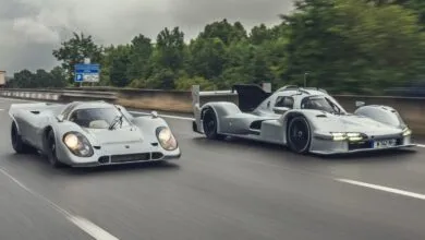 Two silver Porsche race cars driving on a highway, one classic and one modern.