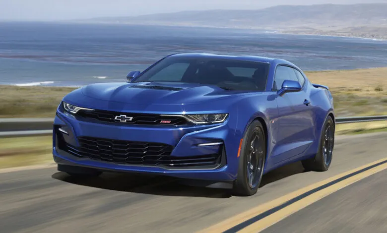 A blue Chevrolet Camaro SS drives along a coastal highway with the ocean in the background.