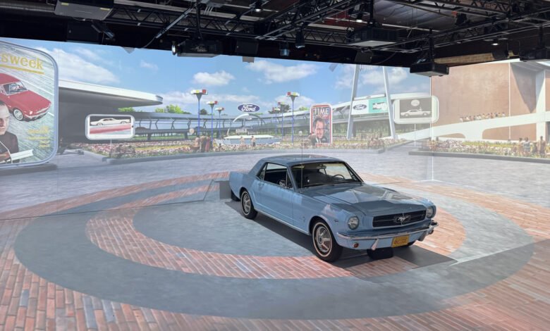 A light blue classic Ford Mustang coupe displayed in front of a projected backdrop.