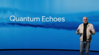 Man in a light jacket and jeans speaking in front of a blue background with the words "Quantum Echoes"