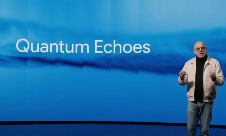 Man in a light jacket and jeans speaking in front of a blue background with the words "Quantum Echoes"