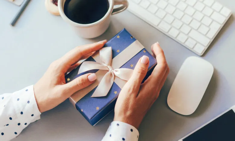 Hands holding a blue gift box with gold stars and a cream ribbon.