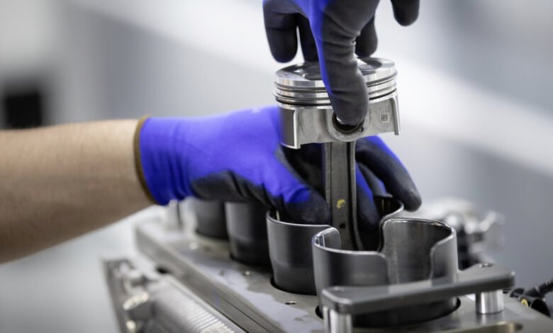 Close-up of gloved hands assembling a piston into an engine block.