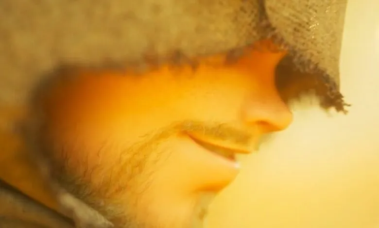 Close-up profile of a person's face with a beard and a burlap hood.
