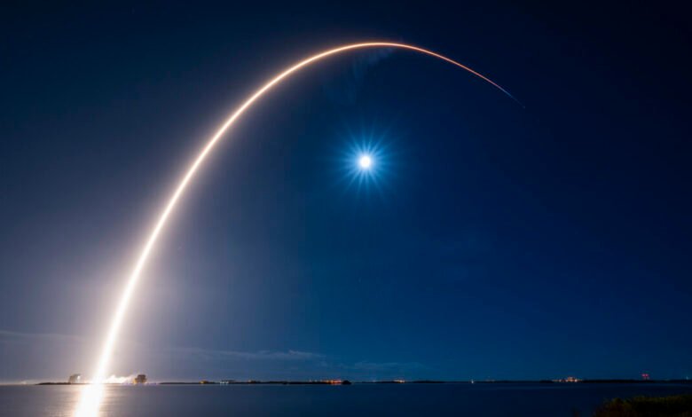 Rocket launch streak against a dark blue night sky with a bright moon.