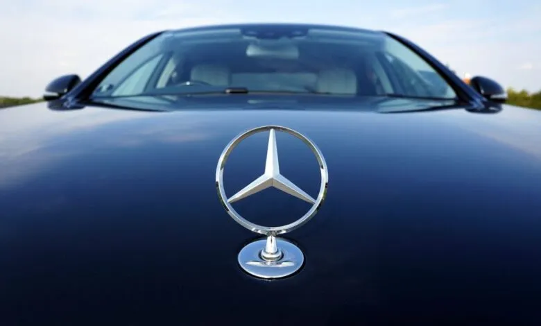 Close-up of the iconic Mercedes-Benz three-pointed star emblem on the hood of a dark car.