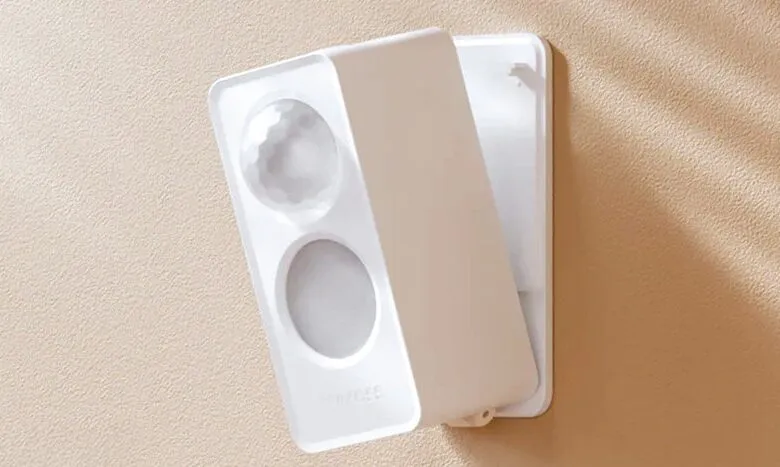 White motion sensor device with two lenses mounted on a textured beige wall.