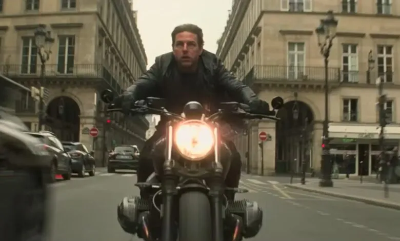 Tom Cruise rides a motorcycle through a Parisian street, looking determined.