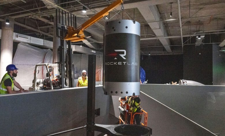 Workers in hard hats and safety vests install a large Rocket Lab component using a crane.