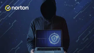 Person in a dark hoodie holding a laptop displaying a cyber security shield icon.