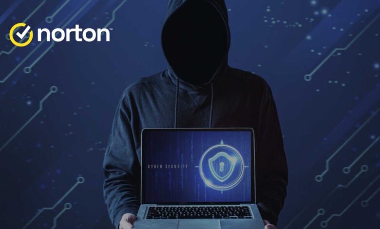 Person in a dark hoodie holding a laptop displaying a cyber security shield icon.
