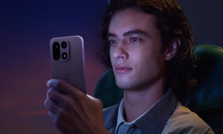 Young man holding a purple OnePlus smartphone in a dimly lit setting.