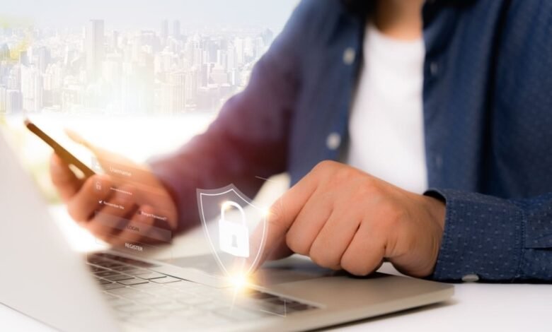 Person using a laptop and smartphone with a digital lock icon overlay, symbolizing cybersecurity.