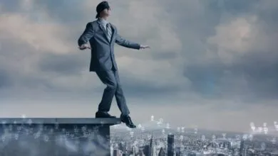 Blindfolded businessman walking on the edge of a building overlooking a city.