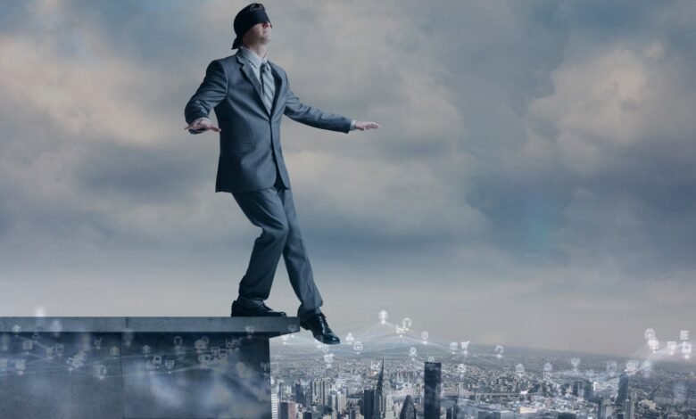 Blindfolded businessman walking on the edge of a building overlooking a city.