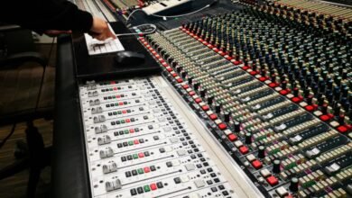 Close-up of a large audio mixing console with a hand on a keyboard.