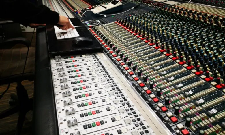 Close-up of a large audio mixing console with a hand on a keyboard.
