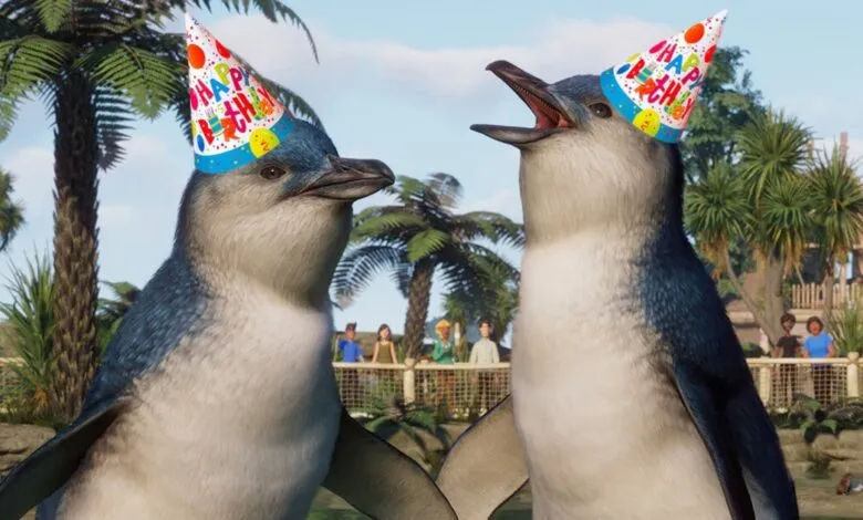 Two penguins wearing birthday hats in a zoo enclosure with palm trees.