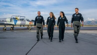 Four astronauts in flight suits walk on an airport tarmac next to a jet.